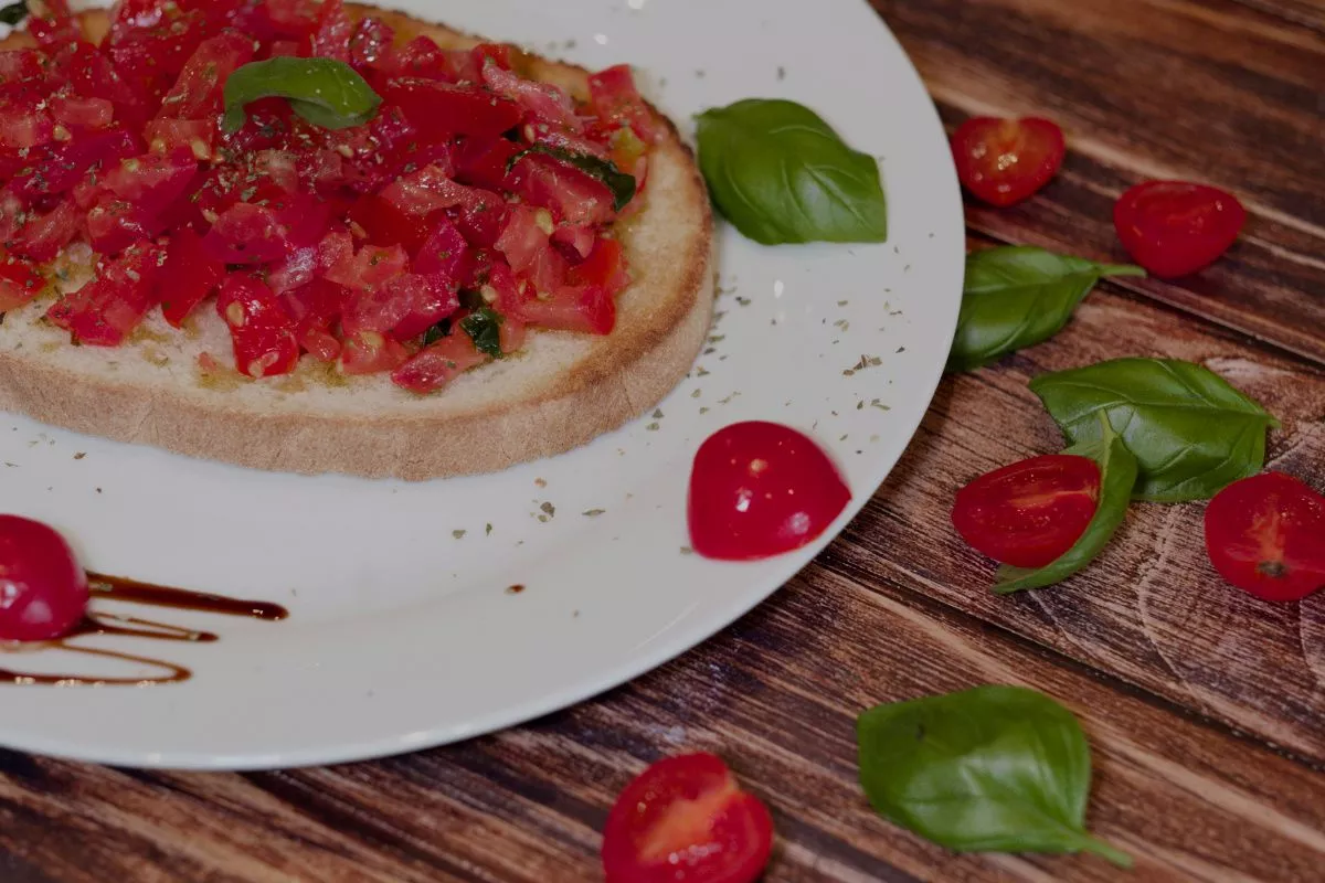 Bruschettan mit Tomaten und Basilikum verziert auf einem weissen Teller.